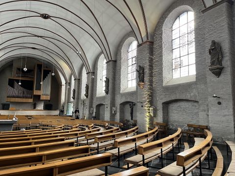 Eine helle Kirche mit hohen Fenstern und einer beeindruckenden Decke. Die Bänke sind aus Holz und bieten Platz für viele Besucher.