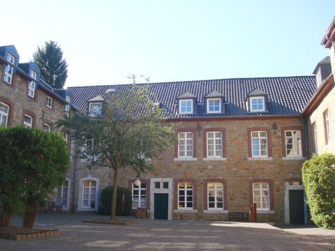 A historic building with a warm stone facade and many windows. In the courtyard, there are some trees and it is sunny.