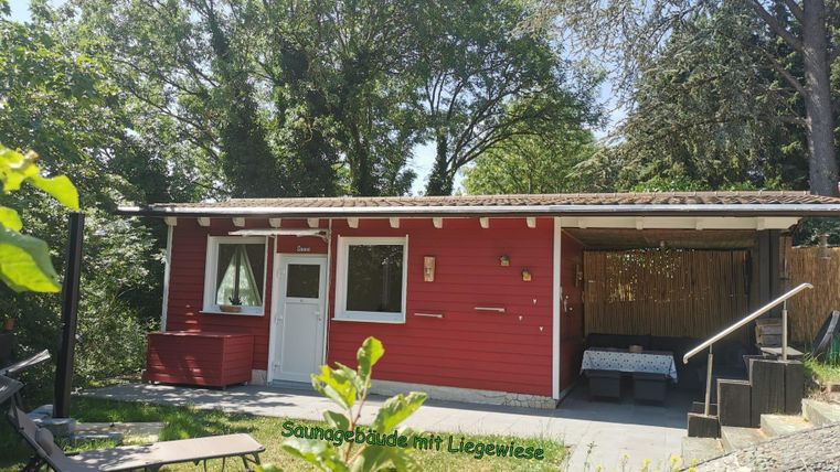 Een rood vakantiehuis in een groene omgeving met een ligweide. Het terras is uitgerust met ligstoelen en biedt een mooi uitzicht op de natuur.