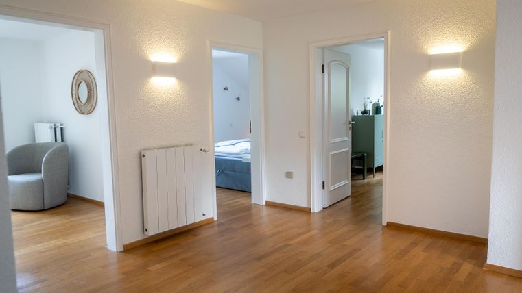 Eine helle, moderne Wohnung mit zarten Wänden und einem warmen Holzboden. Es gibt mehrere Türen zu verschiedenen Räumen und eine gemütliche Sitzecke.
