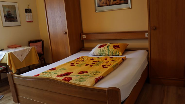 Ein gemütliches Schlafzimmer mit einem Holzbett und einer bunten Decke. An der Wand hängen Bilder und es gibt eine kleine Sitzecke mit einem Tisch.