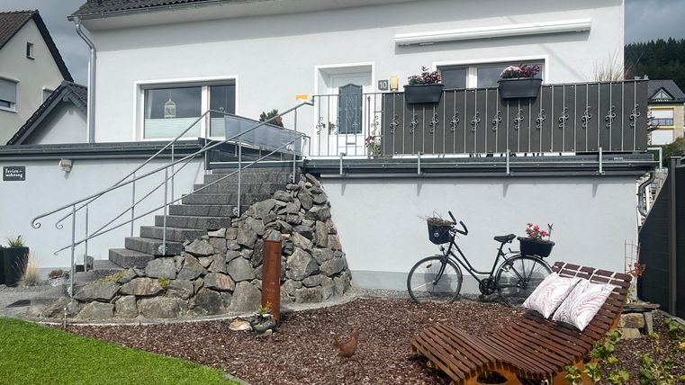 Ein modernes Haus mit Solarpanelen auf dem Dach. Der Garten ist gepflegt, mit einer Steintreppe und einem Fahrrad.