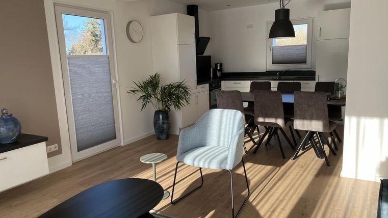 Ein modernes Wohnzimmer mit einem Essbereich. Helle Farben, minimale Möbel und große Fenster sorgen für eine freundliche Atmosphäre.