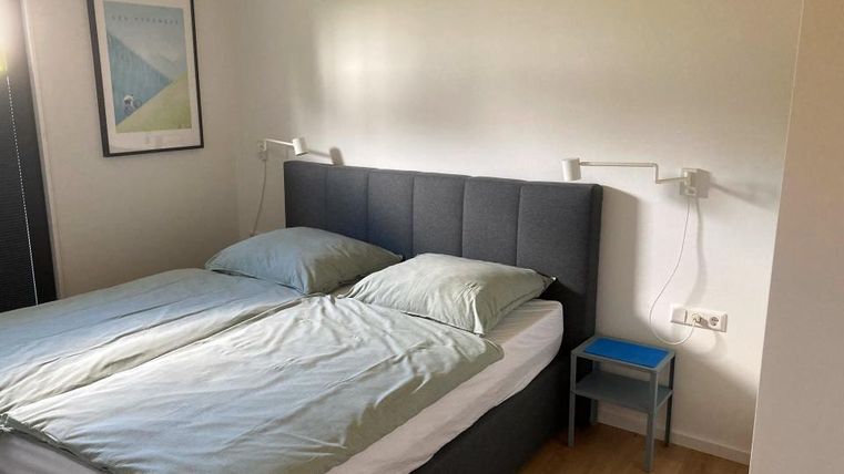 Ein schlichtes Schlafzimmer mit einem großen Bett und grauen Bettdecken. Neben dem Bett steht ein kleiner Nachttisch und es sind moderne Wandlampen installiert.