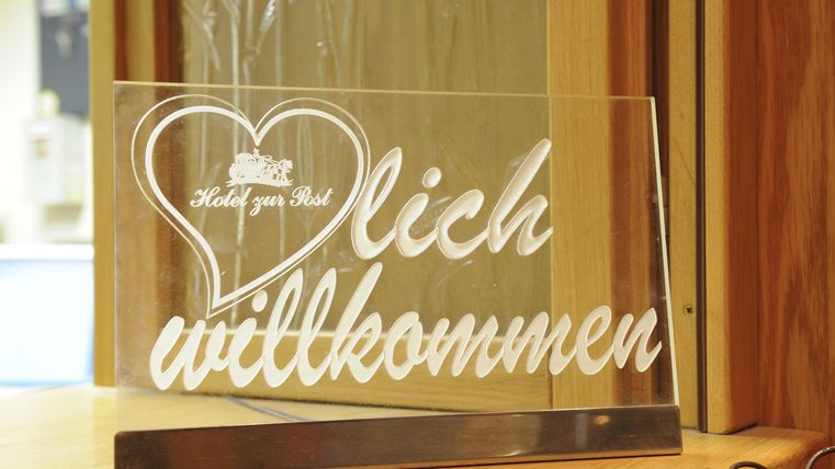 Ein dekoratives Willkommensschild aus Glas mit einer herzförmigen Gestaltung. Der Text "lich willkommen" ist in einer eleganten Schriftart eingeprägt.