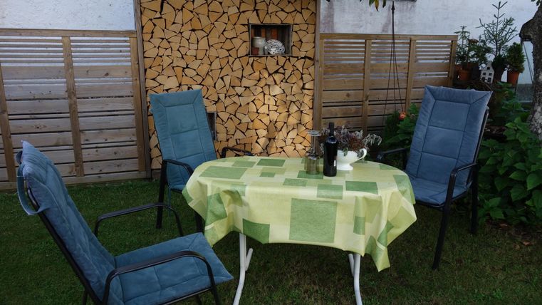 Een gezellige tuin met een tafel en vier stoelen. Op de achtergrond staat een houtrek.