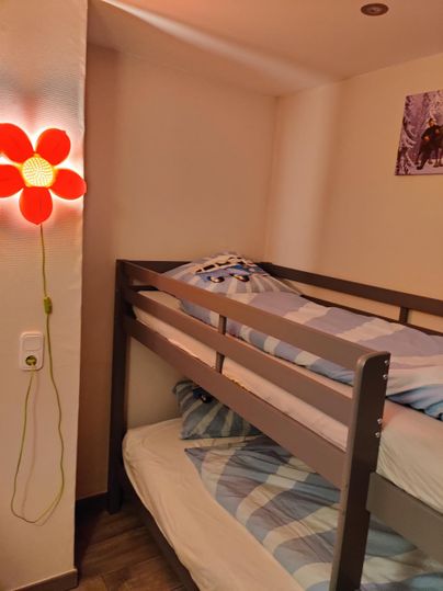 A cozy room with a loft bed and a colorful flower light. The bedding is blue and white.