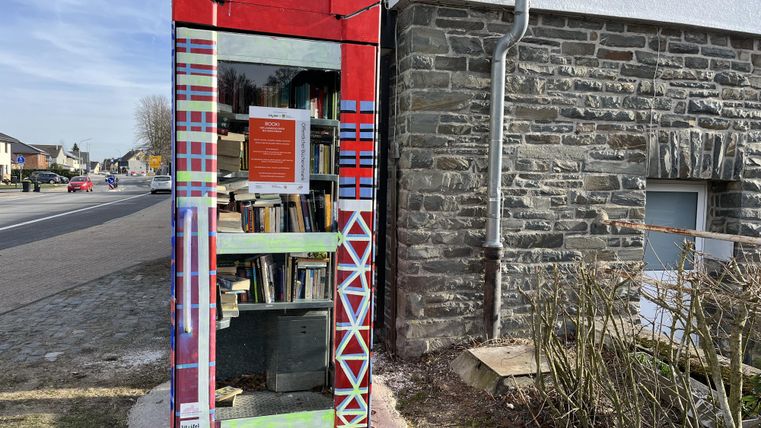 Een kleurrijke boekenbox staat op de straathoek naast een gebouw. Ze is gevuld met verschillende boeken en biedt leesmogelijkheden voor voorbijgangers.