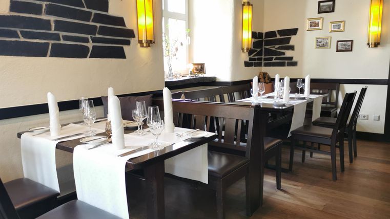 Ein elegantes Restaurant mit holzfarbenen Tischen und Stühlen. Die Atmosphäre ist hell und einladend, ergänzt durch dekorative Wandleuchten.