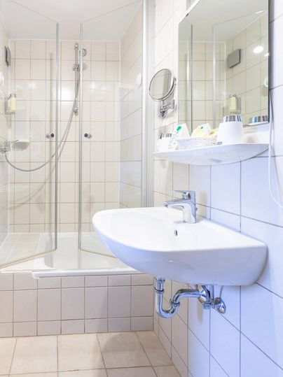 A modern bathroom with a spacious shower and a sink. The walls are tiled and the decor is bright and stylish.