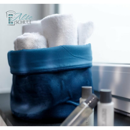 Ein blauer Korb mit mehreren weißen Handtüchern und Pflegeprodukten. Die Szene wirkt sauber und einladend.