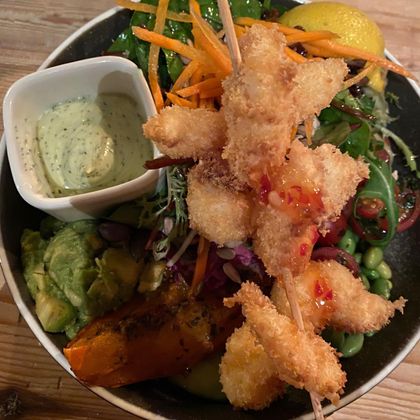 Ein bunter Salat mit knusprigen Garnelen-Spießen. Dazu gibt es eine cremige Sauce und frische Zutaten wie Avocado, Karotten und Zitrone.