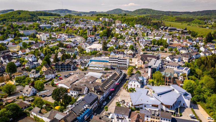 Eine Luftaufnahme einer attraktiven Kleinstadt mit vielen Häusern und grünen Hügeln im Hintergrund. Die Felder und Bäume verleihen der Umgebung eine ruhige und einladende Atmosphäre.