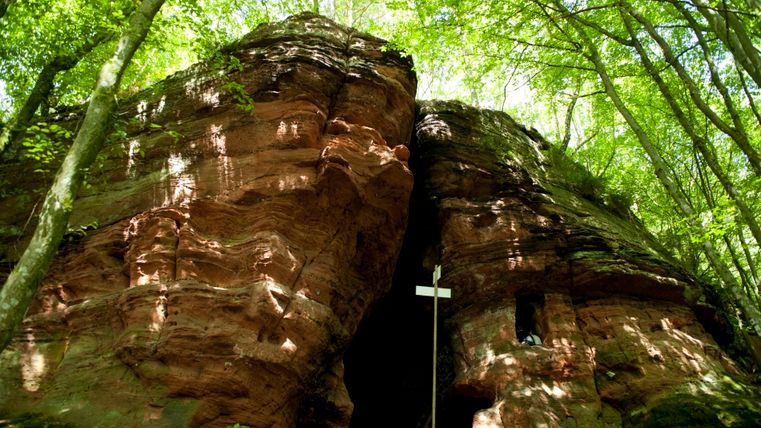 Rock formation with cave in the forest, surrounded by trees.