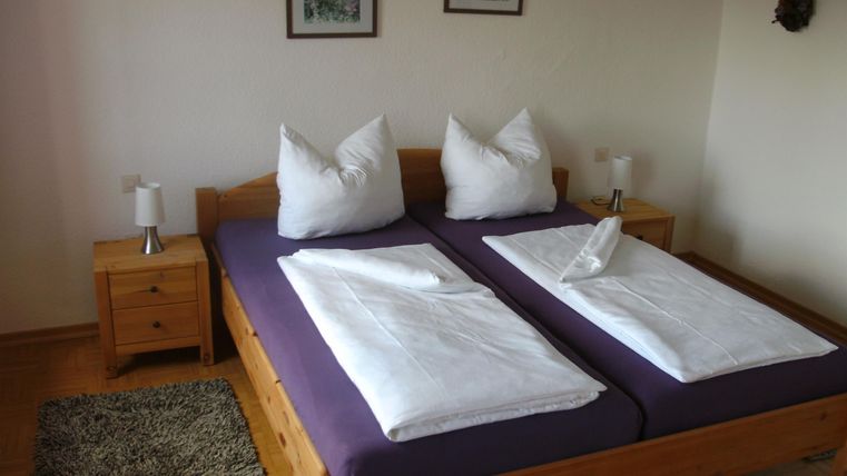 Ein gemütliches Schlafzimmer mit zwei Betten und weißen Kissen. Neben den Betten stehen Nachttische und es gibt dekorative Bilder an der Wand.