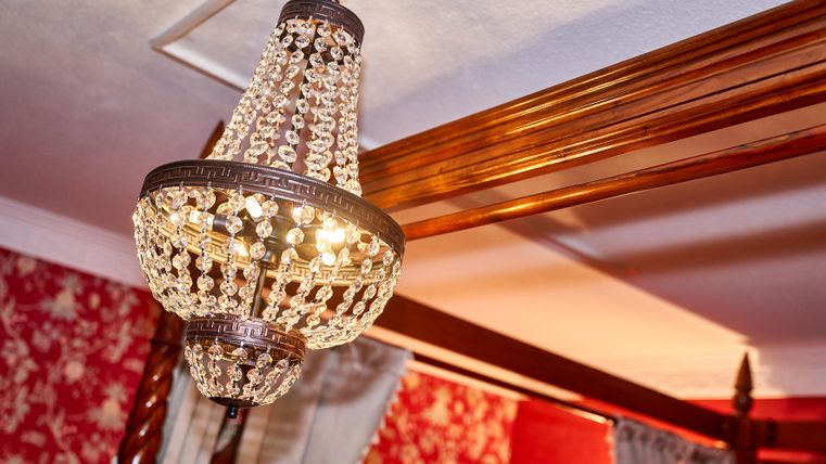 An elegant crystal chandelier hangs from the ceiling. The walls are decorated with a red floral pattern.