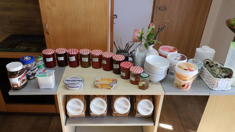 A table with various jars of jam, Nutella, and bowls. In the background, there are flowers and other food containers.