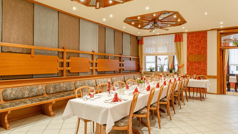 Een elegante eetzaal met lange tafels, die feestelijk zijn gedekt. De wanden zijn voorzien van houten panelen en decoratieve elementen.