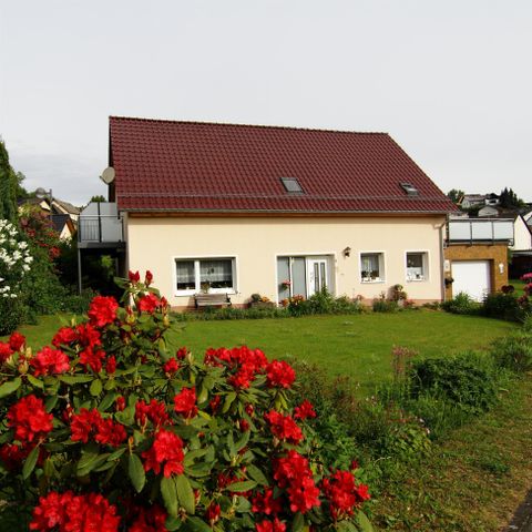 Ein schönes Haus mit rotem Dach und gepflegtem Garten. Im Vordergrund blühen rote Blumen.