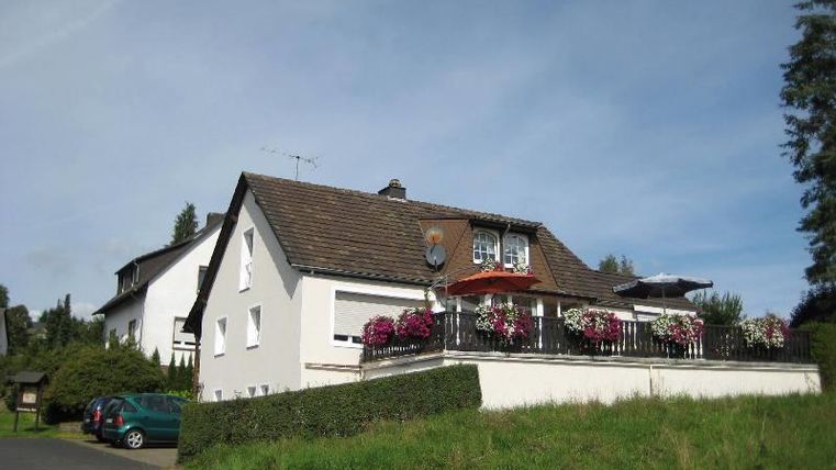 Ein schönes Haus mit einem Balkon, der mit bunten Blumen geschmückt ist. Die Umgebung ist grün und friedlich.