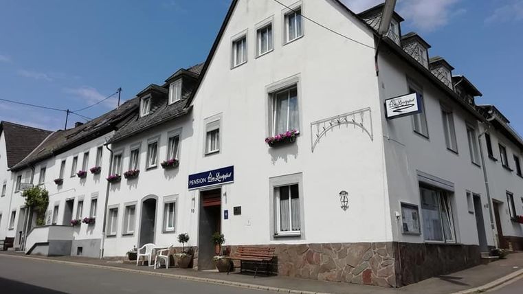 Een wit gebouw met meerdere ramen en bloembakken. Voor het huis staan stoelen en een tafel op straat.