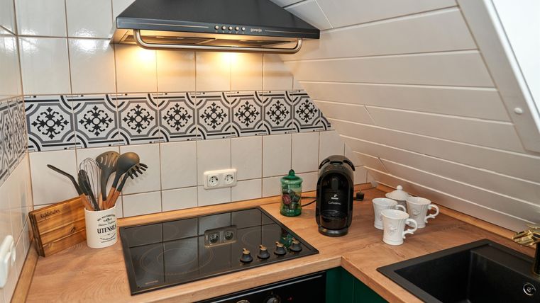 A modern kitchen with a wooden countertop and an elegant tile backsplash. There is a cooktop, a coffee machine, and kitchen utensils on the countertop.
