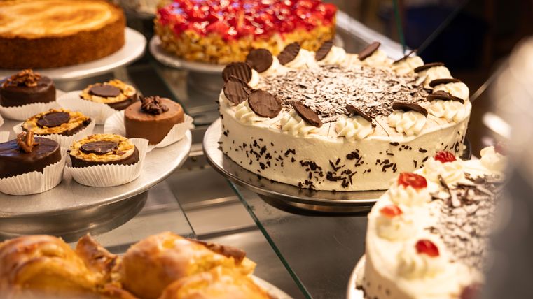 Eine Auswahl von köstlichen Kuchen und Gebäck. Besonders hervorgehoben ist eine Sahnetorte mit Schokoladenstückchen und Kirschen.