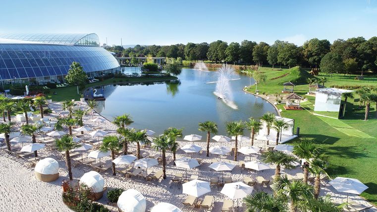 Een mooie park met een meer en palmstoelen. Op de achtergrond staat een kas en er is een kleurrijk tuingebied.