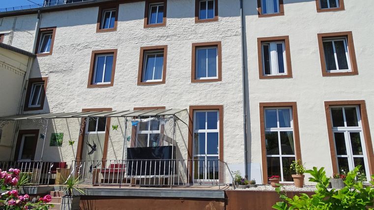 Ein modernes Haus mit vielen Fenstern und einem Balkon. Blumen schmücken den unteren Bereich der Fassade.