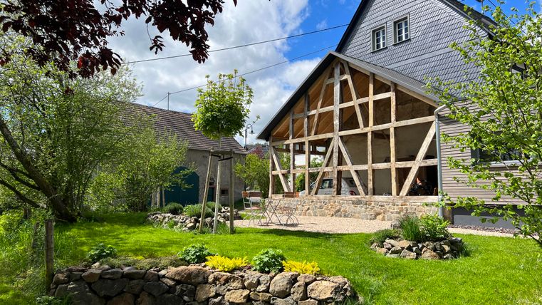 Ein hübsches Haus mit Fachwerk und einem großen Garten. Der Garten ist grün und einladend, umgeben von Bäumen und Sträuchern.