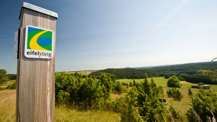 Aussicht vom Kalvarienberg über die Eifel mit Eifelsteig-Wegweiser im Vordergrund.