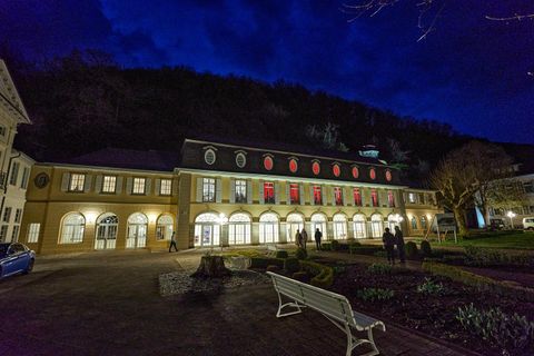 Ein historisches Gebäude bei Nacht, umgeben von einem gepflegten Garten. Die Fenster sind beleuchtet und verleihen der Fassade einen einladenden Charme.