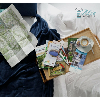 Eine gemütliche Anordnung von Reiseführern und einer Landkarte auf einem Tisch. Dazu eine Tasse Kaffee und eine warme Decke, die eine entspannte Stimmung vermittelt.