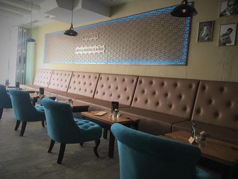 Ein gemütliches Café mit blauen Stühlen und einer gepolsterten Wandbank. Die Atmosphäre ist einladend und modern.