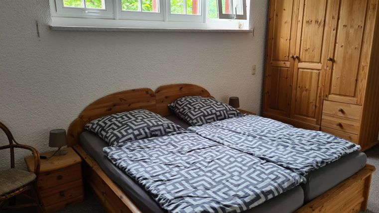 Ein gemütliches Schlafzimmer mit einem Doppelbett und holzverkleideten Möbeln. Großzügige Fenster lassen viel Tageslicht herein.