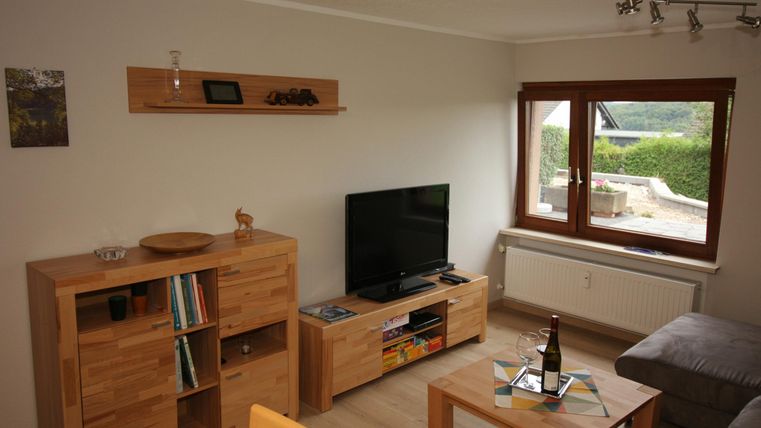 Een gezellige woonkamer met houten planken en een televisie. Grote ramen laten veel licht binnen.