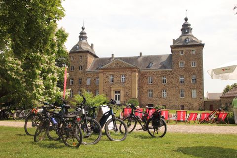 Een indrukwekkend kasteel met een mooie tuin. Op de voorgrond staan meerdere fietsen.