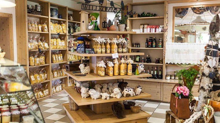 Een gezellige winkel met houten planken die verschillende producten zoals jam, sap en decoraties aanbieden. Op een grote tafel in het midden zijn extra artikelen zoals knuffeldieren en planten gedecoreerd.