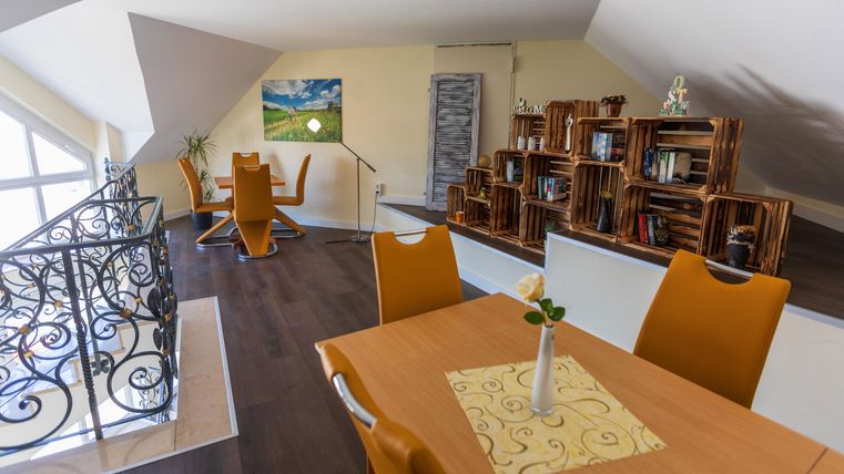 Ein modernes, lichtdurchflutetes Zimmer mit einem Holzregal und einem Esstisch. Die Wände sind hell und es gibt einen schönen Ausblick durch die Fenster.