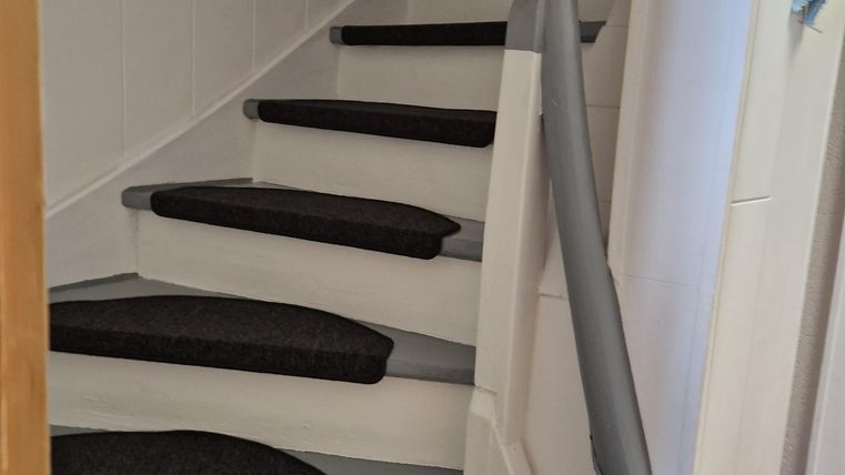 Een trap met grijze treden en antisliploopvlakken. De muren zijn licht en de leuning is elegant vormgegeven.