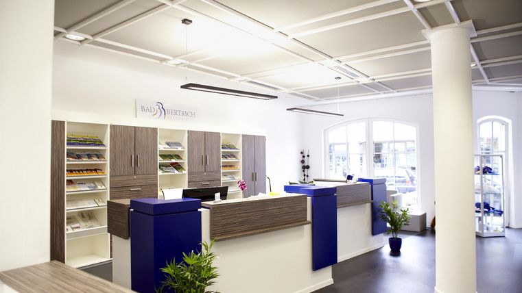 Een moderne receptie met lichte muren en een ruime sfeer. Bij de receptie staan blauwachtige meubels en enkele planten decoreren de ruimte.