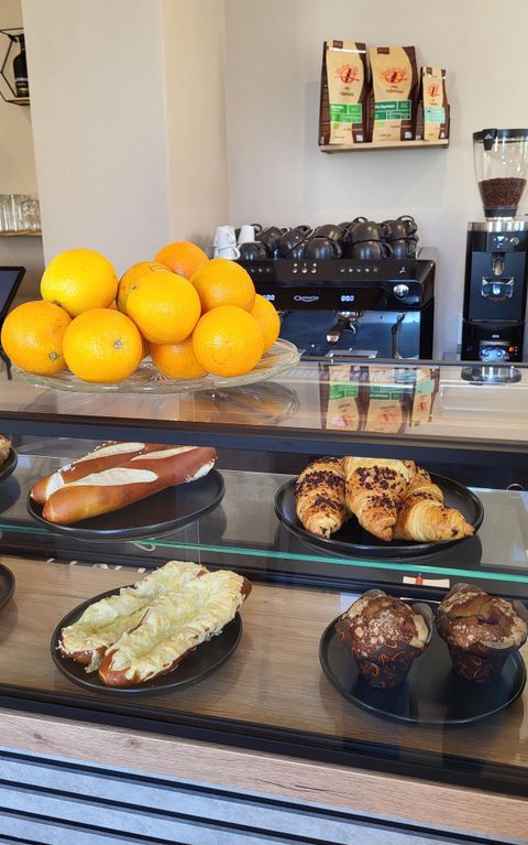 Een gezellige cafébar met verse sinaasappels en verschillende bakkerijproducten. In de aanbieding zijn pretzels, croissants en muffins.