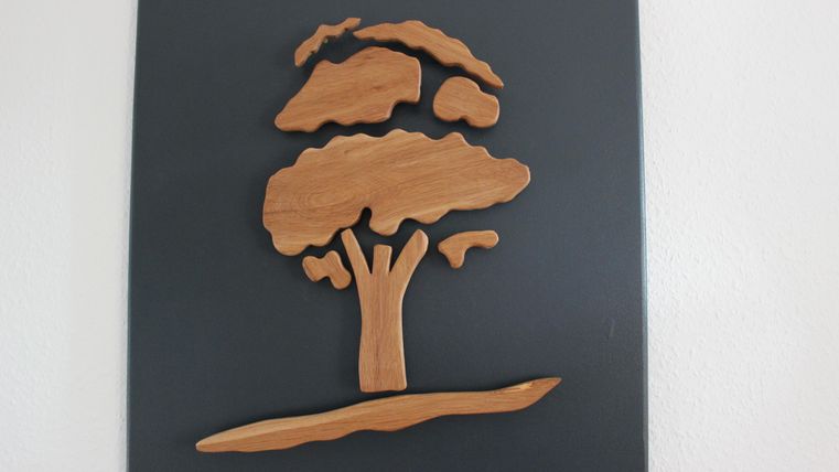A wood sculpture of a tree on a black surface. The tree has a stylized shape with fluffy leaves and a sturdy trunk.
