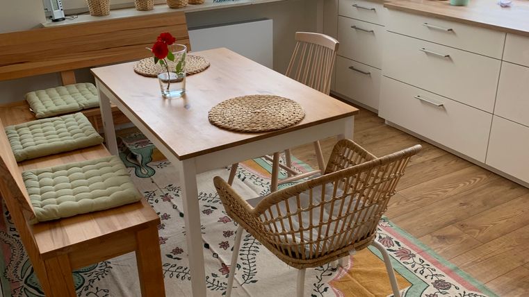 Een gezellige eetruimte met een houten tafel en rieten stoelen. De ramen zijn licht en planten brengen frisheid in de ruimte.