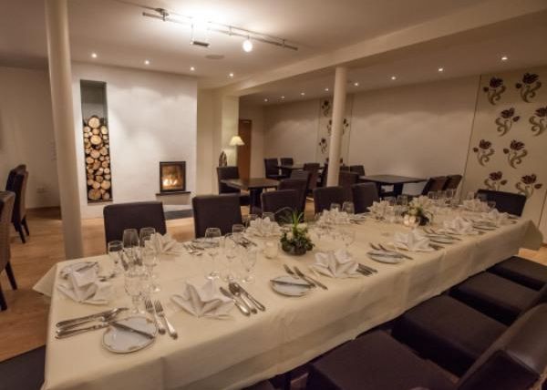Een elegante eetkamer met een feestelijk gedekte tafel. Op de achtergrond staat een open haard en de muren zijn smaakvol gedecoreerd.