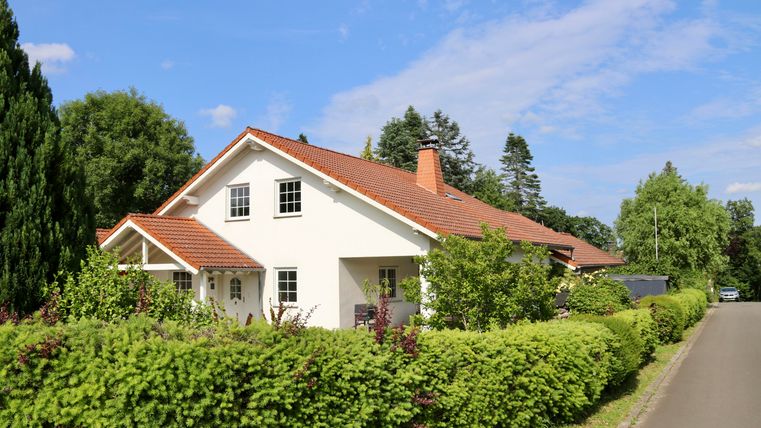 Een mooi eengezinswoning met een rood dak en een groene tuin. De straat is rustig en omzoomd met bomen.