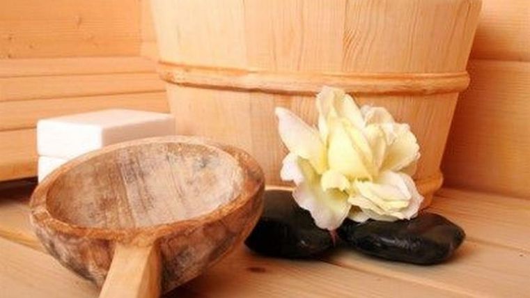 Eine entspannende Saunatmosphäre mit einem Holzlöffel, einem Eimer, Seifenstücken und einem weißen Blütenblatt. Die warmen Holzfarben und der Zen-Charakter laden zur Erholung ein.