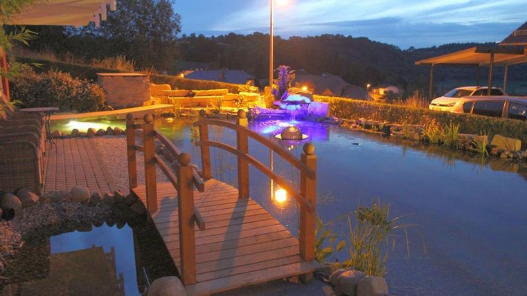 Ein schöner Garten mit einem Holzsteg über einem ruhigen Teich. Sanftes Licht und Pflanzen schaffen eine entspannende Atmosphäre.