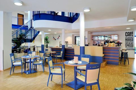 Een modern café met blauwe en witte elementen. Tafels en stoelen nodigen uit om te blijven zitten, terwijl de balie op de achtergrond zichtbaar is.