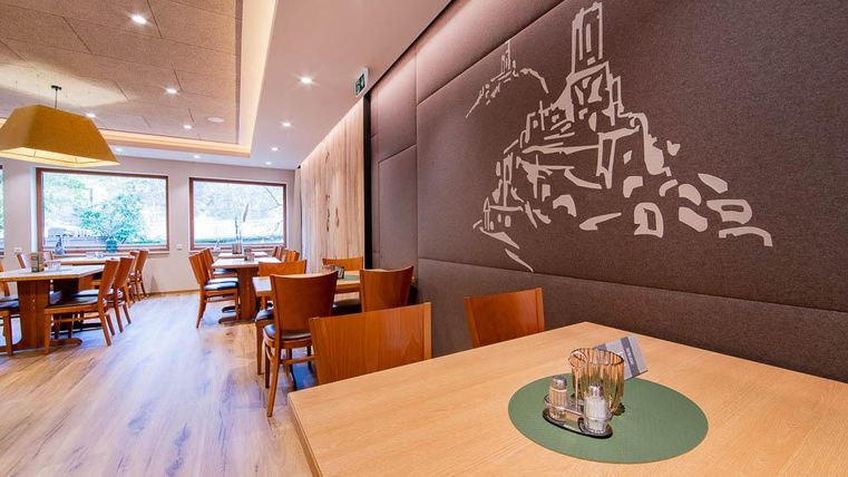 Ein modernes Restaurant mit Holzmöbeln und eleganter Dekoration. An der Wand ist eine künstlerische Darstellung eines historischen Gebäudes zu sehen.